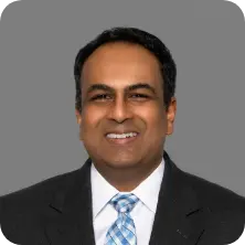 Professional headshot of Raj, smiling, wearing a suit and tie. Business portrait.