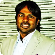 Portrait of Riyaad, a man with dark hair, wearing a light-colored blazer and a light blue shirt.