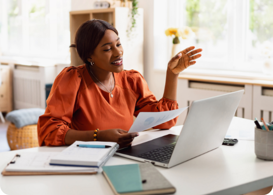 TPAs-banner A woman in an orange blouse smiles while video chatting on a laptop at a bright home office. Papers, notebooks, and a pen are on the desk, creating a friendly and productive atmosphere.